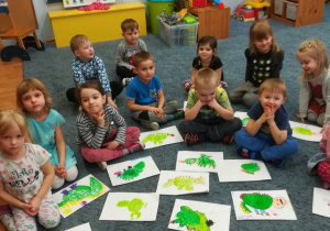 Dzieci siedzą na dywanie prezentują rysunki smoków.